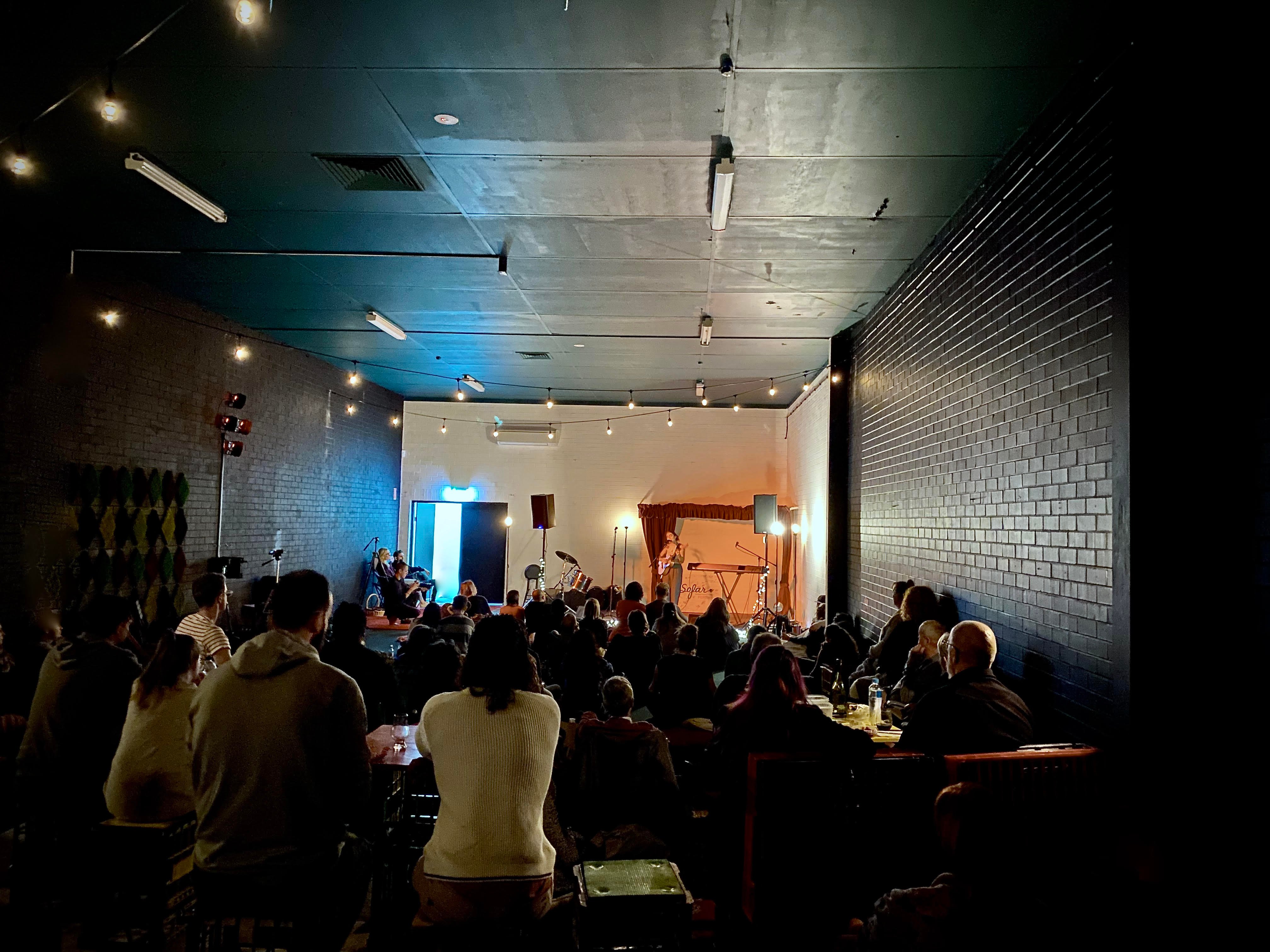 Small music gig in a dark space with festoon lights and a crowd