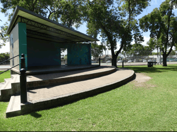 Curved outdoor stage sound shell surrounded by lawn and trees, available to hire through SpacetoCo