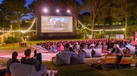 Outdoor cinema screening at night with a crowd seated on beanbags under string lights
