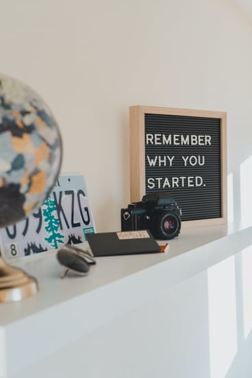 Shelf styled with a globe, license plate, camera, notebook and a letterboard reading "remember why you started"
