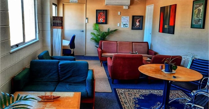 Community lounge room with mismatched velvet sofas in blue and burgundy, wooden coffee tables, framed art on the walls and layered rugs