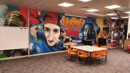 Ellenbrook Community Library youth hyperlab with a hip hop mural, orange chairs and communal tables, available to book on SpacetoCo