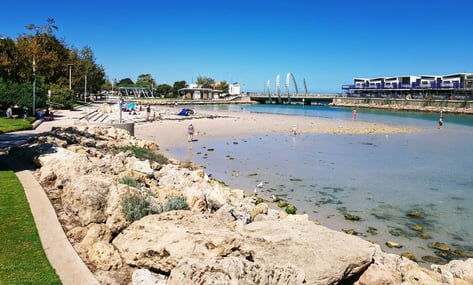 Ngarkal Beach shoreline with limestone rocks, calm water and a pedestrian bridge in the background