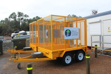 Orange trailer cage on a dual axle, parked outdoors with Shire of Serpentine Jarrahdale logo visible on the side panel, available to hire through SpacetoCo